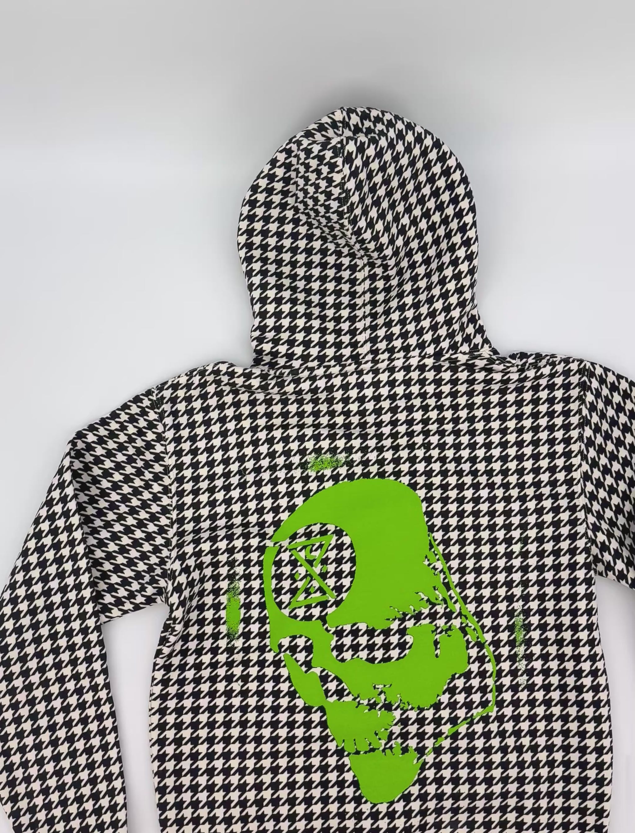 video of a black and white houndstooth hoodie with a neon green skull graphic of the ghostship outer banks skull
